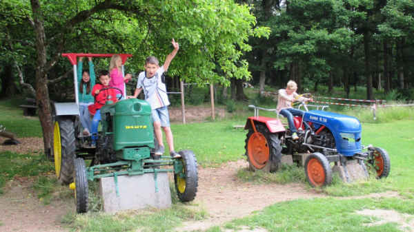 Drei Kinder spielen auf alten Traktoren.