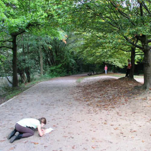 Ein Kind hockt im Wald auf dem Boden und macht Notizen.