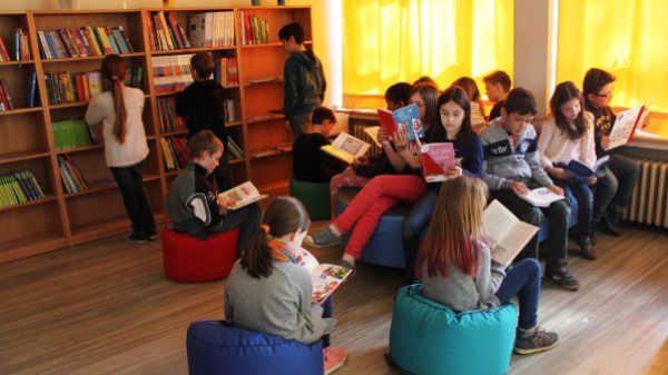 Einige Kinder sitzen in der Bücherei auf einem Sofa und Hockern und lesen.